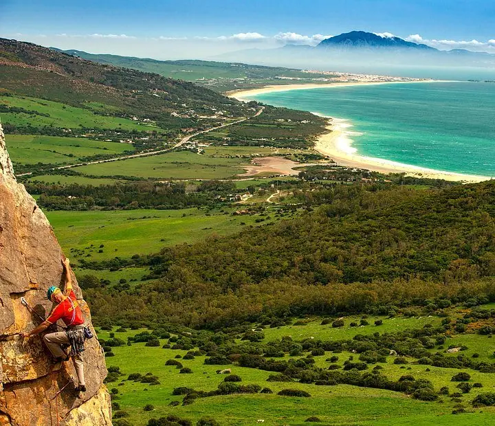 Grimpeuse sur une falaise dominant une vallée verte et la mer